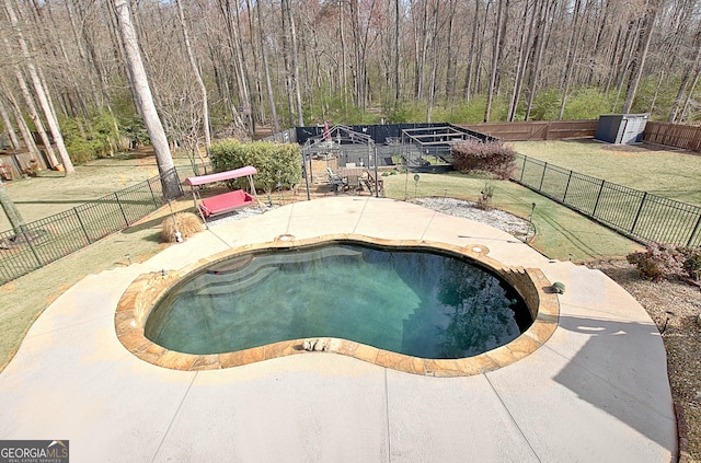 view of swimming pool featuring a fenced in pool, a forest view, a lawn, a fenced backyard, and a patio