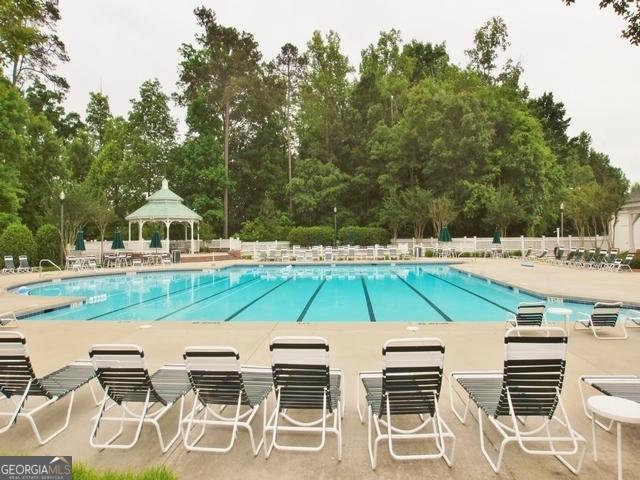 community pool featuring a gazebo, a patio area, view of wooded area, and fence