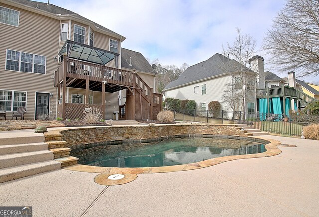 outdoor pool featuring a wooden deck, a patio, stairs, and fence