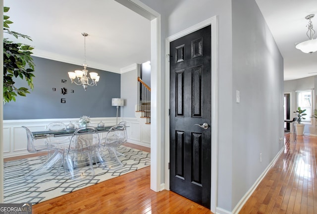 hall with wood-type flooring, stairway, wainscoting, a chandelier, and a decorative wall