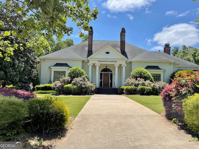 greek revival inspired property featuring a chimney, a front lawn, and a shingled roof