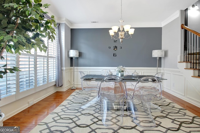 dining space featuring wood finished floors, stairway, a chandelier, ornamental molding, and wainscoting