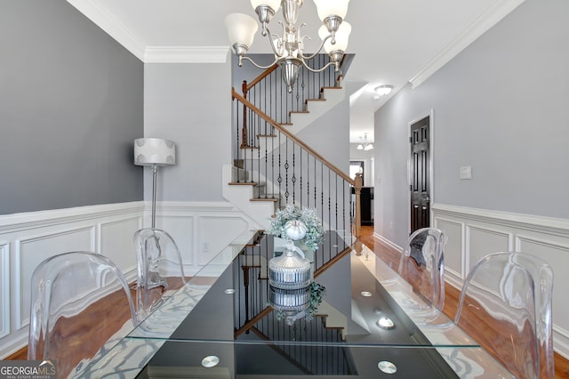 dining space featuring a chandelier, crown molding, a decorative wall, a wainscoted wall, and stairs