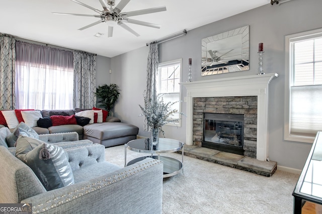 carpeted living room featuring ceiling fan, a stone fireplace, and baseboards