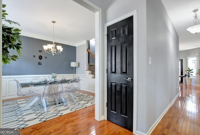 interior space featuring a wainscoted wall, ornamental molding, hardwood / wood-style flooring, an inviting chandelier, and stairs