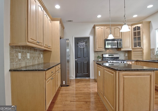 65 Tapestry Ln, Newnan, GA 30265 - kitchen with stainless steel appliances, light brown cabinets, light wood finished floors, a kitchen island, and dark stone counters