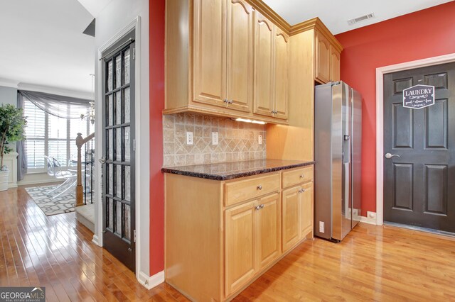 kitchen featuring stainless steel fridge with ice dispenser, light wood-style floors, backsplash, baseboards, and dark stone counters