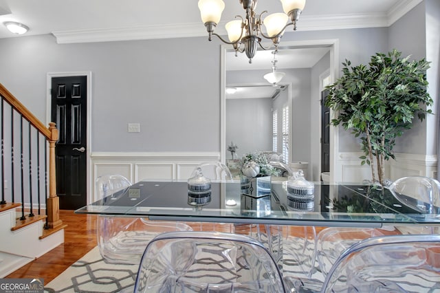 interior space with a wainscoted wall, ornamental molding, wood finished floors, a decorative wall, and a chandelier