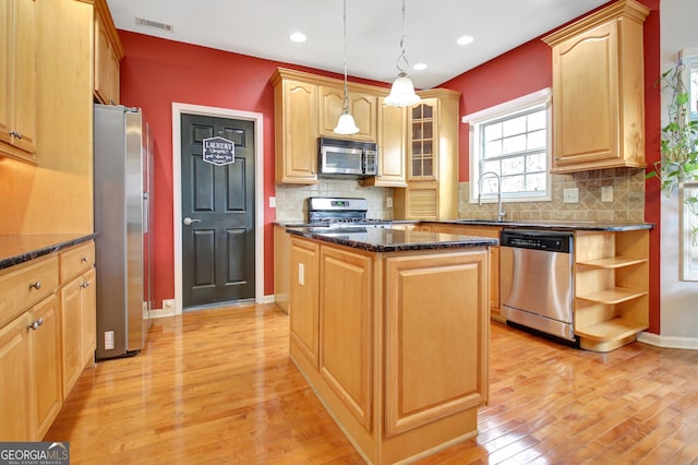 kitchen with stainless steel appliances, light wood-style floors, a center island, a sink, and dark stone countertops