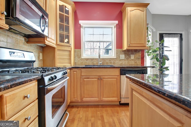 kitchen featuring stainless steel appliances, a sink, light wood-type flooring, glass insert cabinets, and plenty of natural light