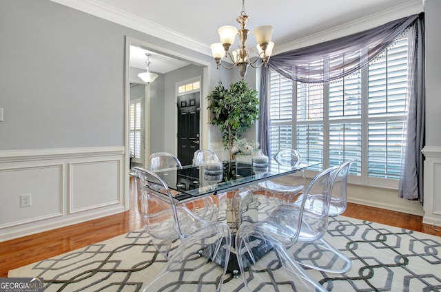 dining area featuring wood finished floors, a wainscoted wall, ornamental molding, a decorative wall, and a notable chandelier