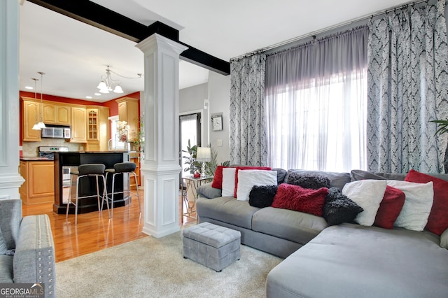 living area with beam ceiling, decorative columns, light wood-style floors, light carpet, and a chandelier