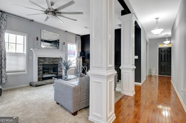 living room with decorative columns, baseboards, a stone fireplace, and a ceiling fan