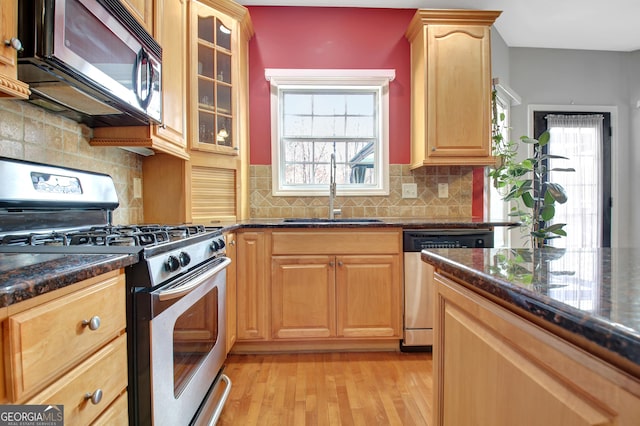 kitchen featuring a sink, backsplash, stainless steel appliances, light wood finished floors, and glass insert cabinets