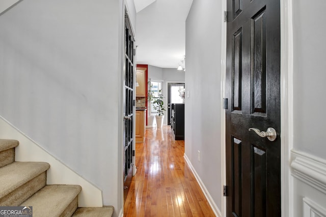 corridor with stairway, light wood-style floors, and baseboards