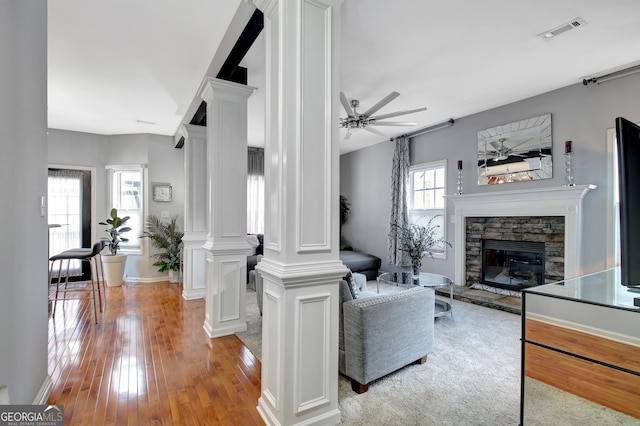 living room with visible vents, ornate columns, a fireplace, light wood-style floors, and a ceiling fan