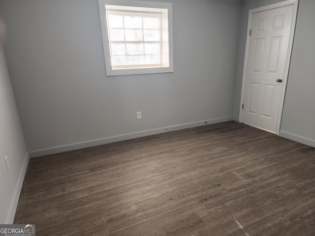 spare room with baseboards and dark wood-style flooring