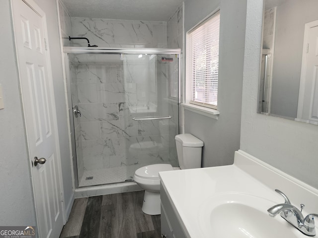 bathroom with a marble finish shower, toilet, vanity, and wood finished floors