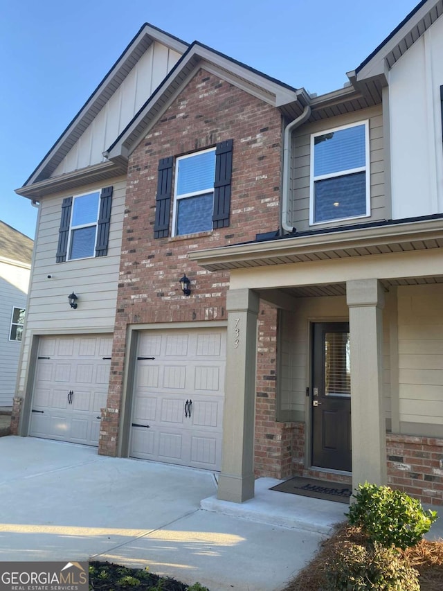 view of front of home with board and batten siding, an attached garage, brick siding, and driveway