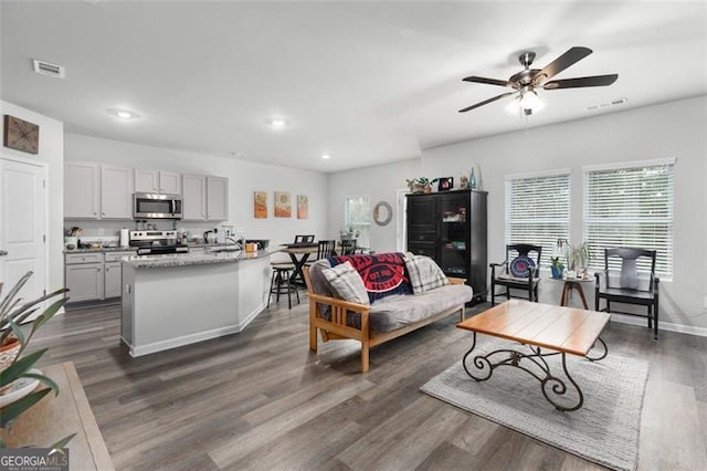 living room featuring visible vents, baseboards, ceiling fan, and dark wood-style flooring