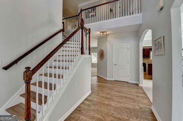 stairs featuring a high ceiling, wood finished floors, arched walkways, and baseboards