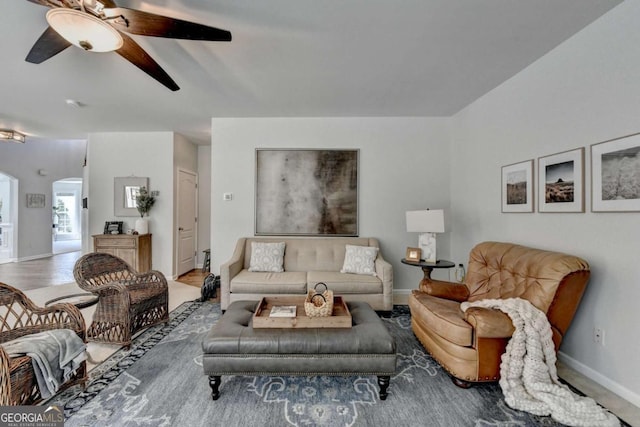 living area featuring wood finished floors, baseboards, arched walkways, and ceiling fan