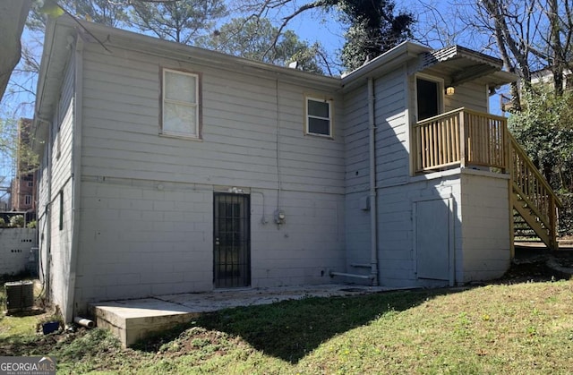 rear view of property featuring stairway, central AC unit, concrete block siding, and a yard