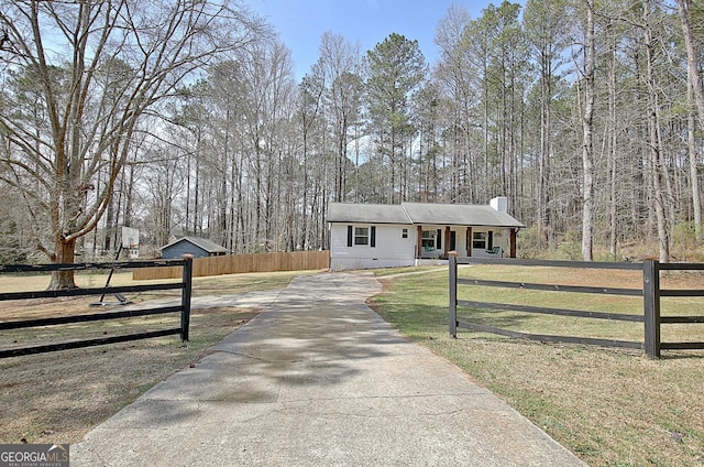 view of front of home with a front lawn, a fenced front yard, a view of trees, concrete driveway, and a chimney