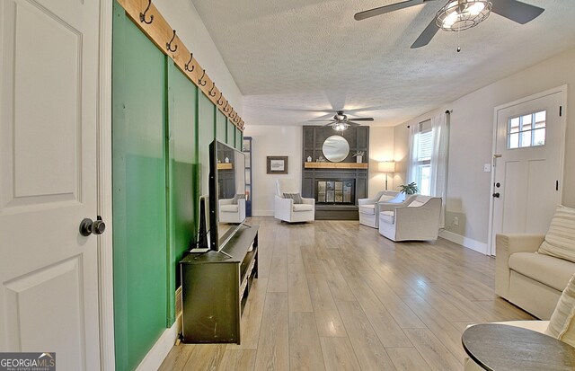 living area with a ceiling fan, baseboards, light wood-style floors, a textured ceiling, and a glass covered fireplace