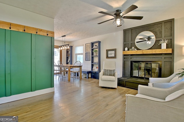 living area featuring ceiling fan with notable chandelier, a textured ceiling, light wood-style floors, and a large fireplace