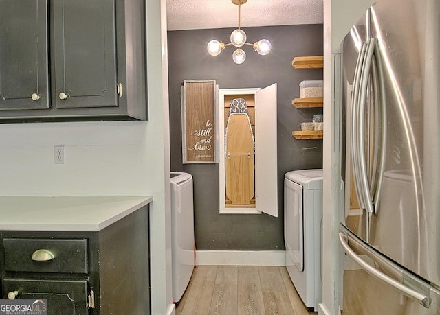 laundry area with a textured ceiling, light wood-style floors, baseboards, laundry area, and washing machine and clothes dryer