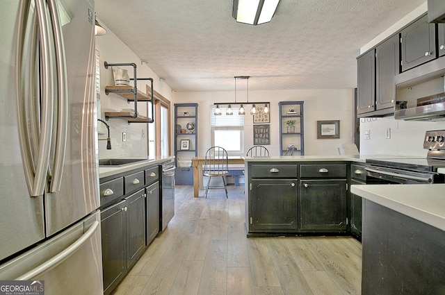 kitchen featuring light wood finished floors, a peninsula, a sink, appliances with stainless steel finishes, and tasteful backsplash