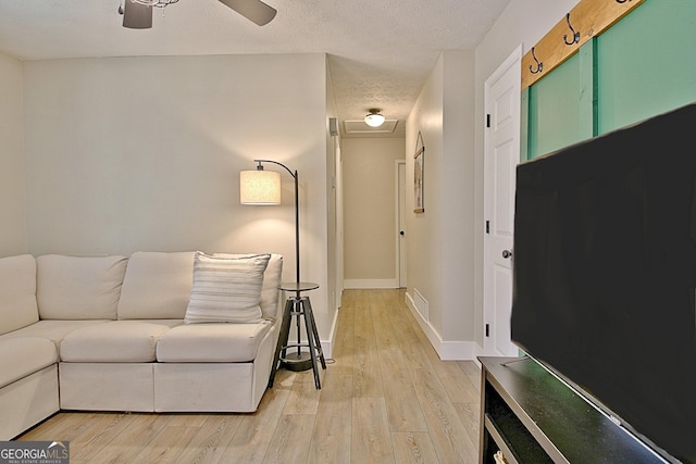 living room with ceiling fan, baseboards, a textured ceiling, and light wood-style flooring