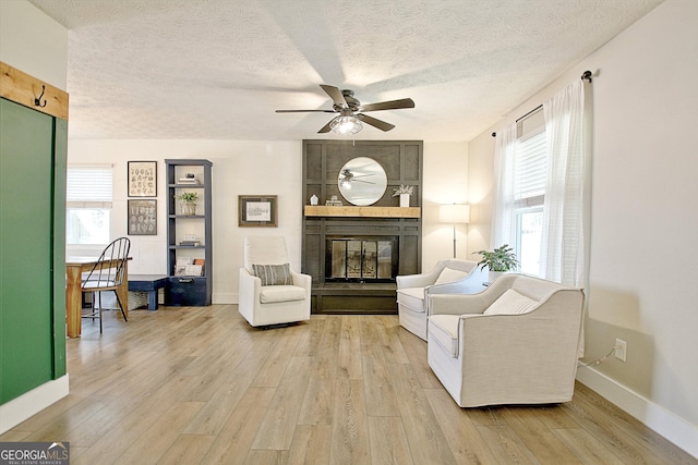 living room featuring baseboards, light wood-type flooring, a fireplace, a textured ceiling, and a ceiling fan