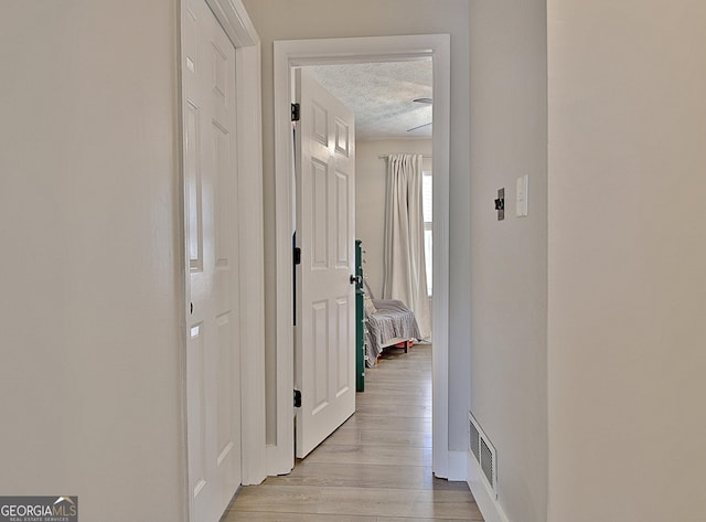 corridor featuring visible vents, a textured ceiling, and light wood-type flooring