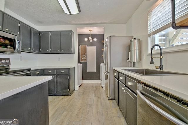 kitchen with light wood-style flooring, a sink, a textured ceiling, appliances with stainless steel finishes, and light countertops