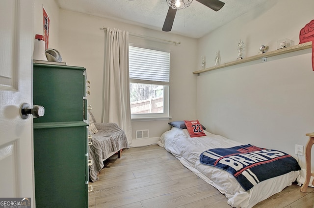 bedroom featuring light wood-type flooring, visible vents, a textured ceiling, and a ceiling fan