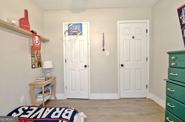 bedroom with baseboards, light wood finished floors, and a textured ceiling