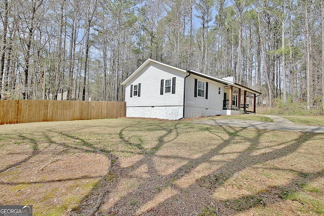 view of front of property with fence, a forest view, a chimney, a front lawn, and crawl space