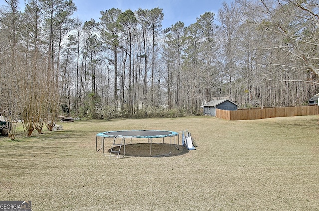 view of yard with an outdoor structure, a trampoline, and fence