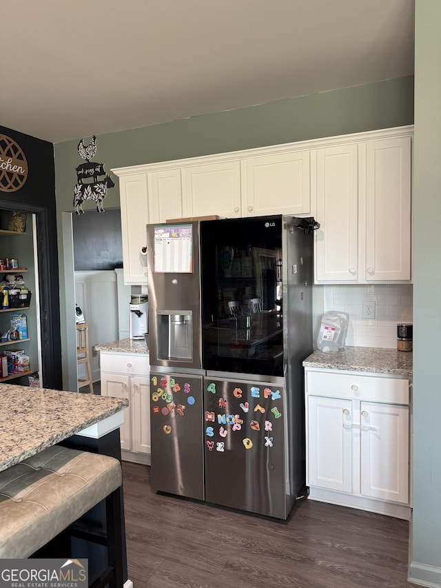 kitchen with dark wood-type flooring, stainless steel refrigerator with ice dispenser, light stone counters, backsplash, and white cabinetry