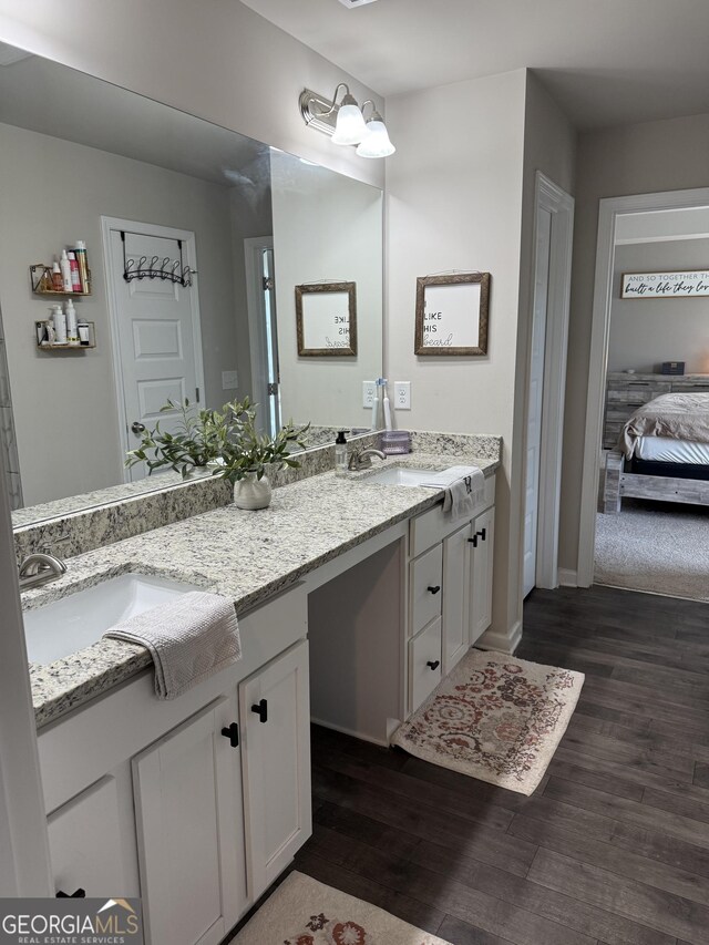 ensuite bathroom featuring double vanity, connected bathroom, wood finished floors, and a sink