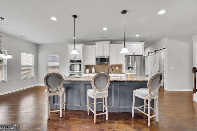 kitchen with backsplash, an island with sink, stainless steel appliances, dark wood-style floors, and white cabinetry