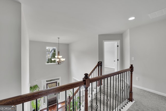 hall with visible vents, an upstairs landing, an inviting chandelier, carpet flooring, and baseboards