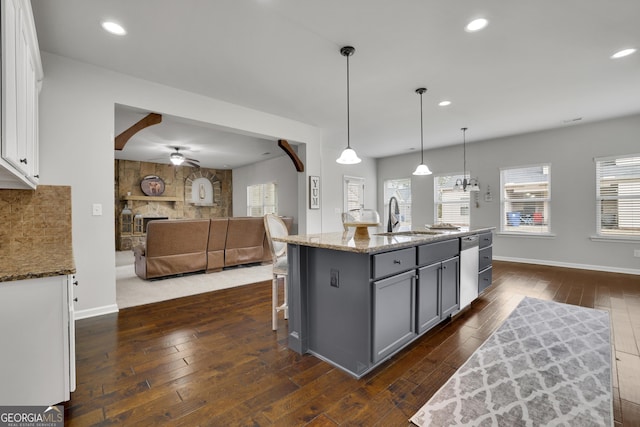 kitchen with gray cabinetry, a sink, stone countertops, open floor plan, and dark wood finished floors