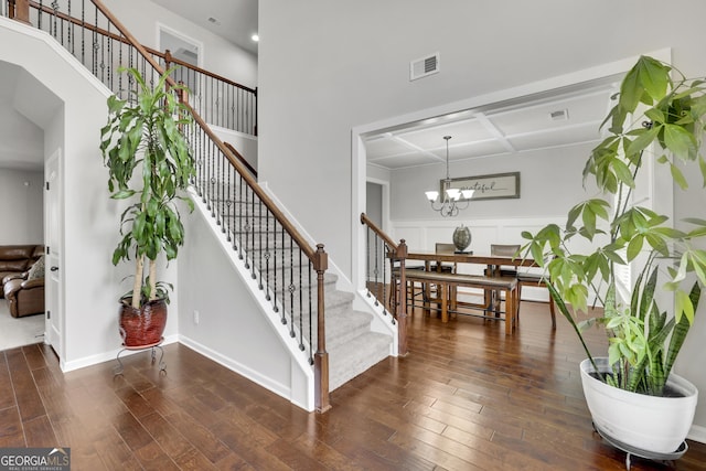 stairway featuring visible vents, a towering ceiling, an inviting chandelier, and wood finished floors