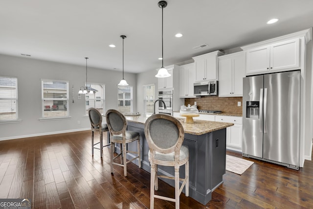 kitchen with visible vents, a center island with sink, light stone counters, appliances with stainless steel finishes, and decorative backsplash