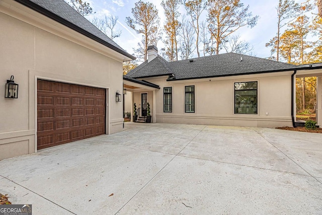 exterior space featuring roof with shingles, an attached garage, driveway, and stucco siding