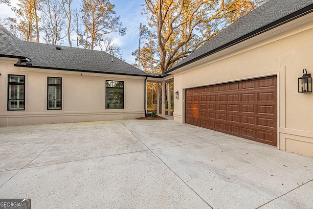 exterior space featuring stucco siding, concrete driveway, and roof with shingles