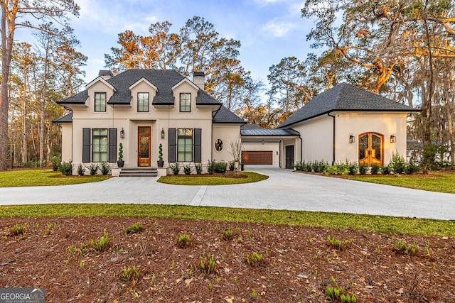 french country style house with an attached garage, a chimney, driveway, and stucco siding